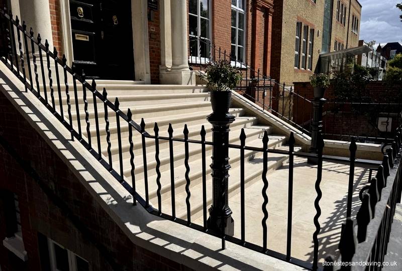 Black iron railings on Portland stone copings above a basement lightwell beside new stone steps